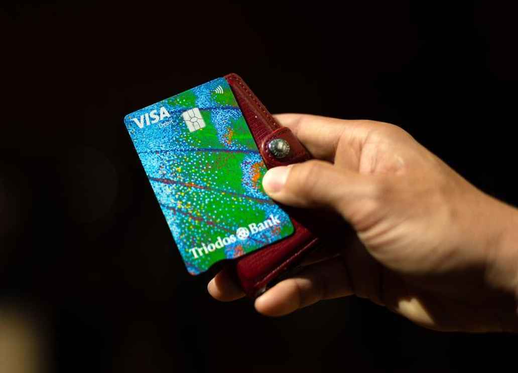Triodos Personal Current Account Card with blue and green butterfly wing design shown held by a held with a brown wallet